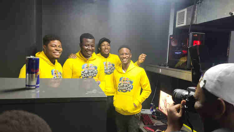 Four men wearing yellow hoodies stand in front of a table.