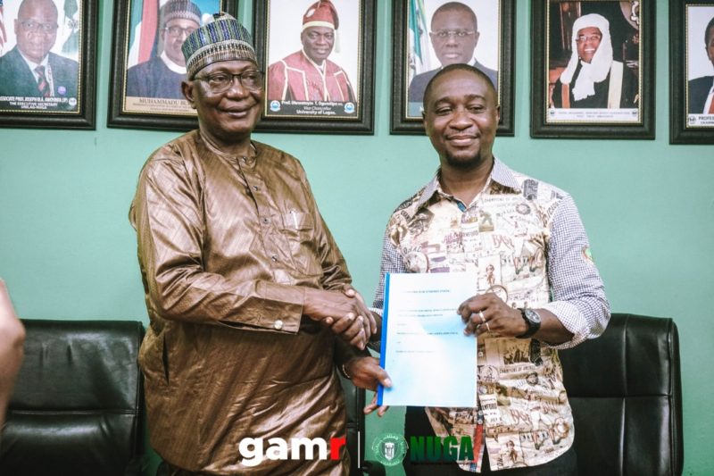 Two men shake hands while holding a blue document.